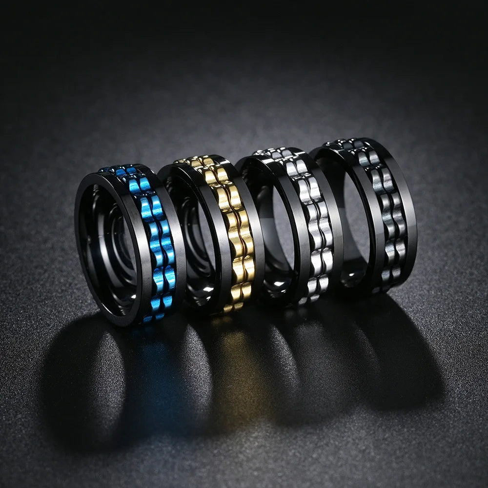 Four metallic rings in black, gold, silver, and blue on a dark textured surface