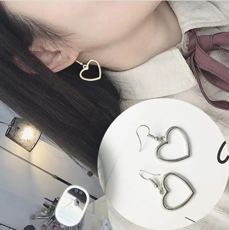 Heart-shaped earrings displayed with a person wearing them indoors.