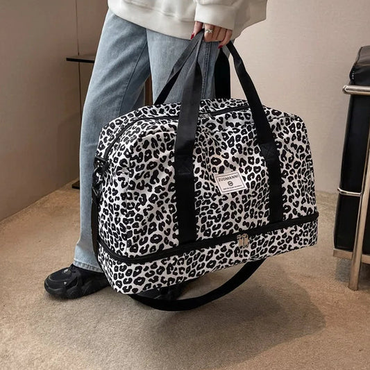 Person holding a leopard print duffel bag in a room with a couch.

