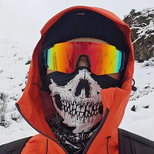 Person wearing a red hooded jacket, colorful ski goggles, and a skull mask in a snowy landscape.