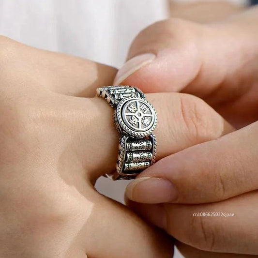 Silver ring with intricate design on a finger against a neutral background