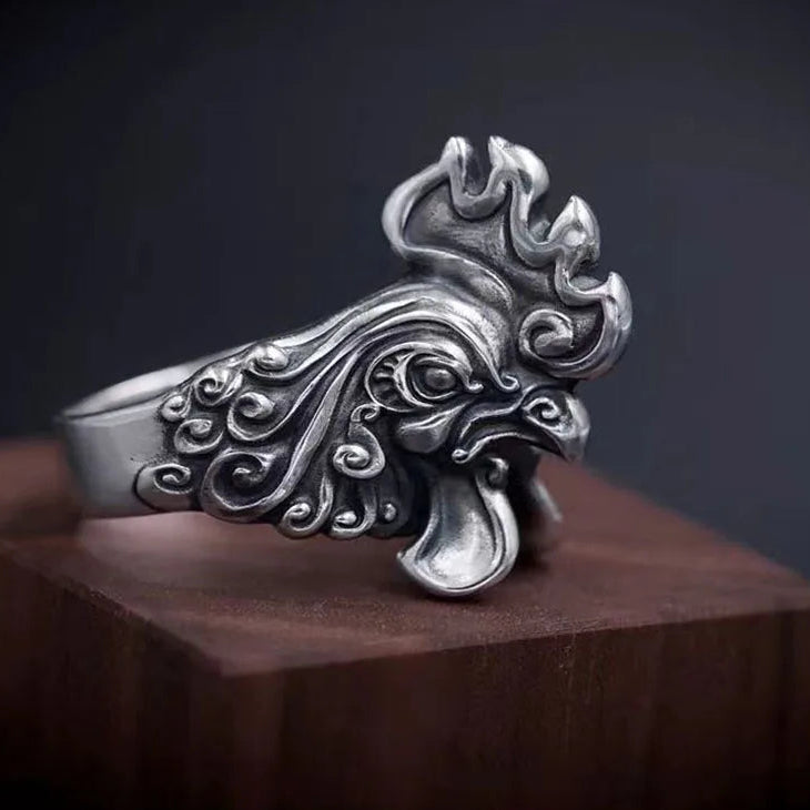 Silver rooster-shaped ring on a wooden block with a dark background